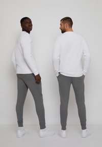 White long-sleeve sweatshirts paired with gray tapered joggers. Both garments have ribbed cuffs, and joggers feature side pockets.