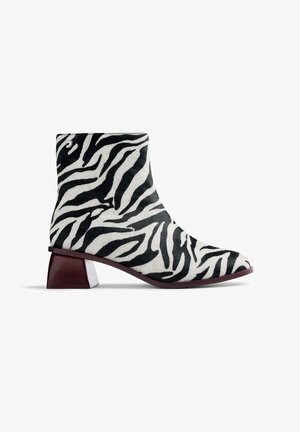 Bottines à imprimé zèbre en matériau synthétique doux, avec un talon bloc effilé et un schéma de couleurs noir et blanc, dotées d'une pointe légèrement pointue.