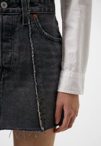 Denim skirt in dark gray with frayed hem, distressed side seam, and raw edges. Paired with a white long-sleeve shirt.