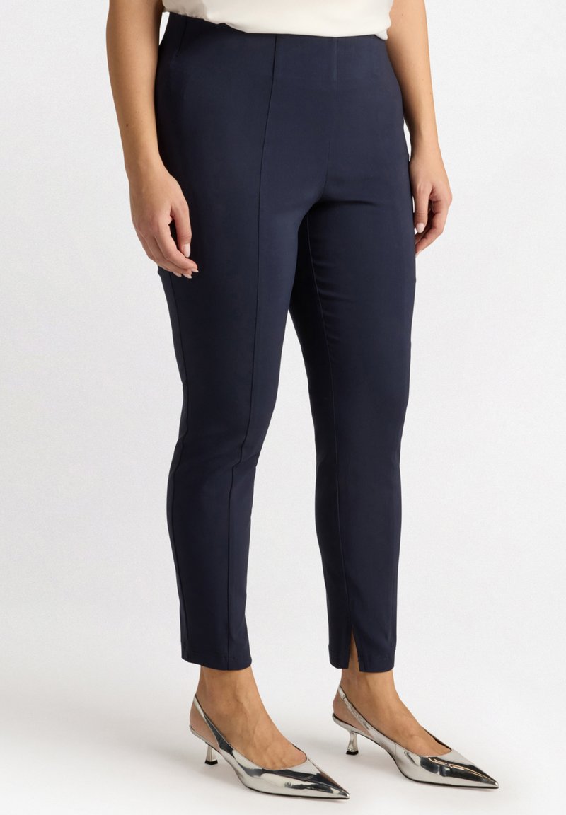 Pantalons slim-fit navy avec une texture lisse, présentant une taille mi-haute, des fentes latérales à l'ourlet, associés à des escarpins argentés à bout pointu.