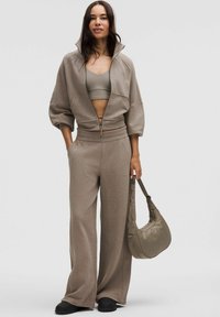 Set de loungewear bej, cu o jachetă cu fermoar scurt și pantaloni cu talie înaltă, având un finisaj texturat. Asortat cu o geantă de umăr corespunzătoare.