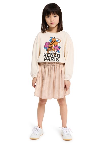 Sweatshirt crème avec imprimé tigre et floral, associé à une jupe rose clair à motif texturé. Des baskets blanches complètent la tenue.