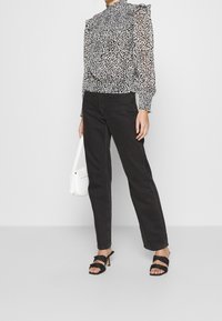 Genomskinlig svart- och vit leopardmönstrad blus med volangdetaljer på axlarna, kombinerad med högmidjade svarta jeans och svarta klacksandaler med remmar.