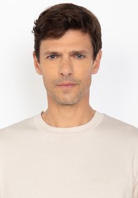 T-shirt beige chiaro a maniche corte realizzato in morbido cotone; presenta un colletto tondo e un logo ricamato discreto sul petto.