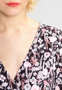 Květinové šaty s hlubokým véčkovým výstřihem, černým pozadím a růžovými, bílými a šedými květinovými vzory; lehký materiál s hladkou texturou.