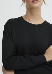 Schwarzes Langarmoberteil mit rundem Ausschnitt und strukturierter Stoff. Verfügt über sichtbare Nahtdetails auf der Vorderseite und enganliegende Ärmel.