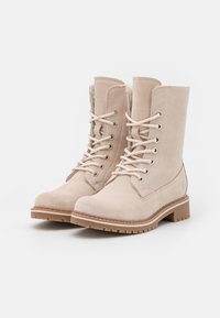 Botas de ante beige con cordones, puntera redonda, ojales de metal y suela de goma texturizada, con un diseño a media pantorrilla y un branding mínimo.