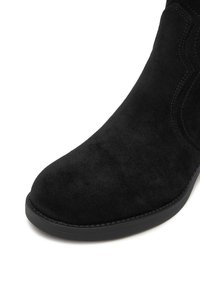 Černé semišové kotníkové boty s kulatou špičkou, hladkým povrchem a kontrastním šitím podél okrajů; lehká gumová podrážka.