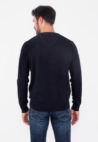 Pulover tricotat de culoare albastru marin, cu mâneci lungi, decolteu rotund și manșete cu nervuri. Textură netedă, cu un siluetă ajustată, văzut din spate.
