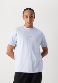 Ljusblå kortärmad t-shirt i bomullsmaterial med en liten logotyp i centrum. Standard rund hals och avslappnad passform.