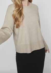 Hellbeiger Pullover mit Rundhalsausschnitt, gerippten Bündchen und Saum. Weicher Stoff und lässige Passform, kombiniert mit einem schwarzen Rock.