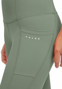 Pantaloni leggings verdi a vita alta realizzati in un tessuto liscio e elasticizzato, con cuciture piatte, tasche laterali e testo del marchio bianco.
