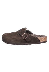 Bruine suede klomp met zachte bontvoering, verstelbare metalen gesp en een kurken tussenzool. Platte zool, ronde neus en naadloos ontwerp.
