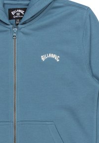 Blauwe hoodie met ritssluiting van zachte stof, voorzien van een kangoeroezak, met een witte geborduurde merkl logo op de borst en een contrasterende rits.
