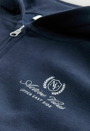 Granatowy sweatshirt z zamkiem błyskawicznym, z białym napisem "Active Vibes Upper East Side" oraz logo w kształcie tarczy z literami "NY", otoczonymi liśćmi laurowymi.
