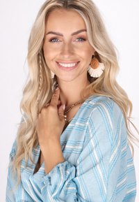 Bluză de un albastru deschis cu modele în zigzag alb și argintiu, mâneci lungi cu manșete plisate, având coliere stratificate și cercei texturați.
