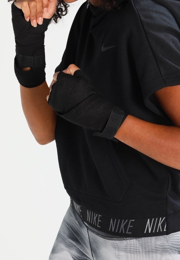 Personne portant des bandes de poignet noires et un haut Nike noir, les mains positionnées en posture de boxe ou de combat.