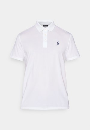 Hvid polo shirt lavet af bomuld, med en klassisk krave, tre-knaps lukning og et marineblåt logo på venstre bryst. Korte ærmer.