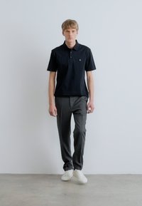 Fekete galléros póló két gombbal, szürke nadrággal és fehér tornacipővel párosítva. Az anyag sima tapintású és testhezálló kialakítású.