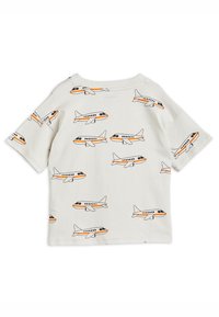 Camiseta de algodón de manga corta en color beige con un patrón de aviones pequeños en todo el tejido, en contornos naranjas y negros. Cuello redondo, corte casual.