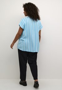 Chemise à manches courtes bleu clair avec des rayures verticales, associée à un pantalon noir et des chaussures noires. Tissu lisse, coupe décontractée et look casual.