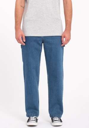 Blue denim cargo pants with a relaxed fit, featuring side pockets and contrasting stitching, paired with a gray t-shirt and black sneakers.