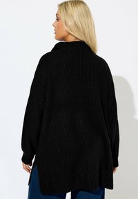 Mustapaitainen neulepaita, jossa on korkea kaulus ja leveät hihat. Ominaisuuksia ovat pystysuuntainen ribbiraidoitus ja sivureiät liikkumisen helpottamiseksi. Sujuva pinta.