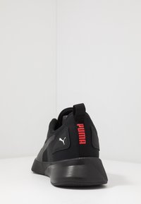 Scarpa sportiva nera con suola testurizzata, caratterizzata da un prominente logo rosso "PUMA" sul tallone e dettagli grigi sui lati.