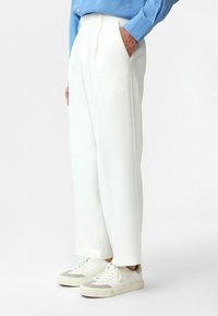 Witte geribde broek met zijzakken, gecombineerd met lichtgrijze en witte sneakers. Het shirt is blauw met een knoopsluiting.