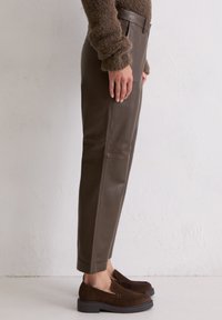Bruine leren broek met een gladde textuur, slim fit en taps toelopende pijpen. Gecombineerd met donkerbruine suède instappers en een chunky gebreide trui.