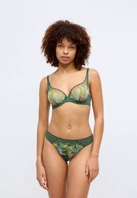 Grön underklädesset med en genomskinlig bh med blommig broderi och matchande lågmidjade trosor. Detaljer inkluderar dekorativa spännen och vågformade kanter.