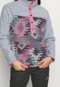 Pullover in felpa grigio con colletto rosa e chiusura a bottoni, caratterizzato da un motivo geometrico colorato in viola, blu e grigio.