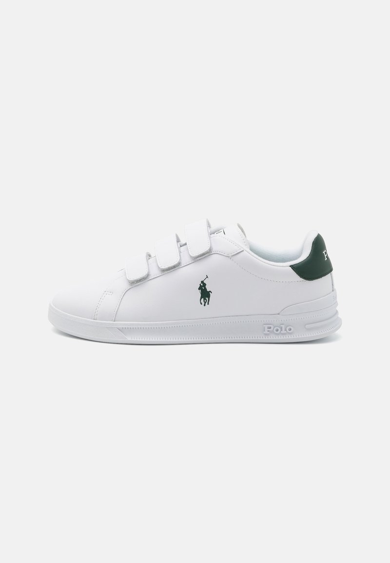 Weißer Sneaker mit Klettverschlussriemen, grünen Akzenten an der Ferse und grünem Logo an der Seite. Glatte Textur, Gummisohle und runde Zehenform.