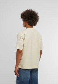Beige bomull t-skjorte med korte ermer og rund hals, som har en avslappet passform og ensfarget tekstur, kombinert med lys blå vide bukser.