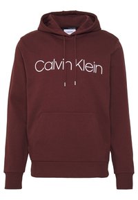 Bordový mikina s kapucí vyrobená z měkké tkaniny, s přední kapsou a bílým logem "Calvin Klein" na hrudi. Žebrované manžety a spodní lem.