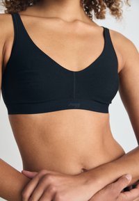 Crni bralet s V-izrezom, napravljen od mekanog materijala, sa bešavnim stilom i glatkom teksturom. Logo je vidljiv na traci.