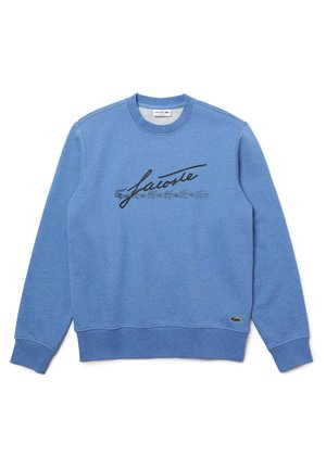 Niebieska bluza z okrągłym dekoltem, z czarnym napisem "Lacoste" i małym zielonym logo krokodyla przy lewym dolnym brzegu.