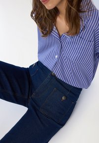 Camicia a righe blu e bianche con bottoni abbinata a jeans a vita alta blu scuro con dettagli in metallo sui bottoni e tasche frontali.