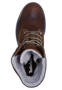 Botín de cuero marrón con un suave forro de felpa gris, puntera redonda y ojales metálicos para los cordones. La suela tiene un diseño texturizado.