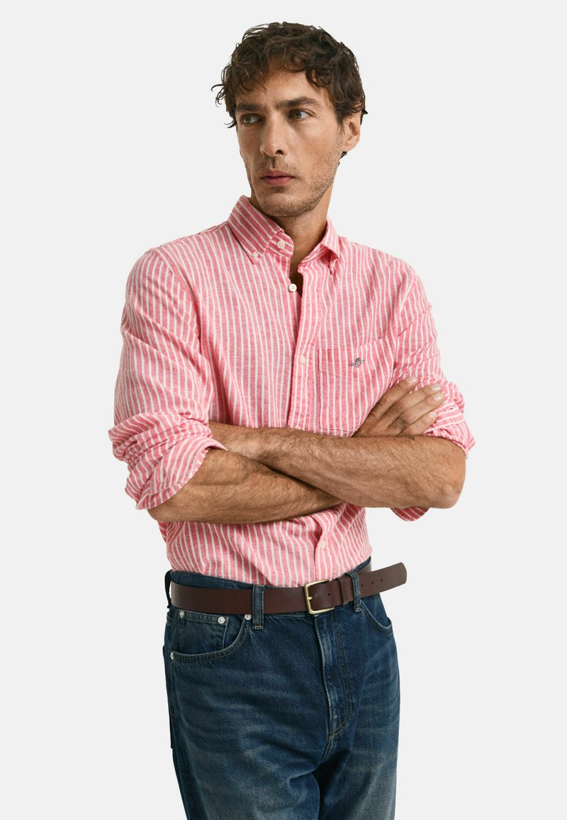 Rood-wit gestreepte overhemd met opgerolde mouwen, gecombineerd met donkerblauwe jeans en een bruine riem. Casual pasvorm, zachte stof.