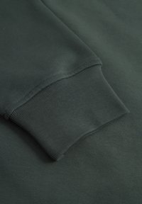 Dunkelgrüner Sweatshirtstoff mit einer strukturierten Oberfläche. Die Bündchen haben einen gerippten Abschluss. Glatte, gleichmäßige Nähte entlang der Kanten.