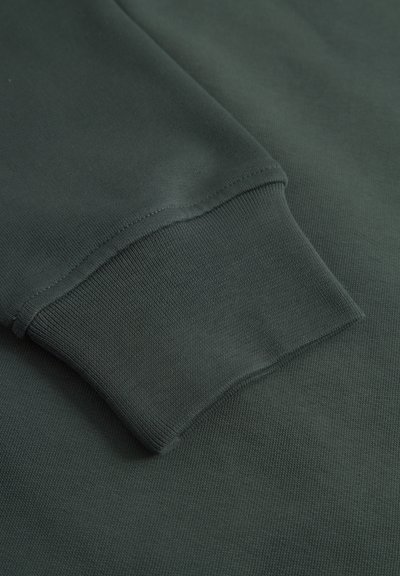 Tissu de sweat-shirt vert foncé avec une surface texturée. Les poignets ont une finition côtelée. Couture lisse et uniforme le long des bords.