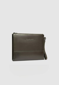 Donkergroene leren tas met ritssluiting, rechthoekige vorm en een gladde textuur. Voorzien van een gedrukt logo en een verstelbare riem.