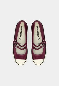 Bordo kanvas kurpes ar divām sprādzēm, noapaļota purngala, melna gumijas zole un balts purngals. Converse zīmols redzams uz zolītes.