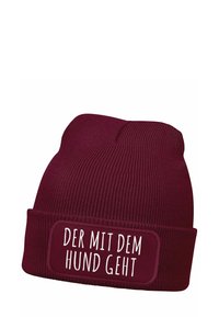 Burgundy knit beanie with a folded cuff. A white rectangular patch displays the text "DER MIT DEM HUND GEHT" in bold font.