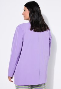 Fialový oversize blazer vyrobený z hladkého materiálu. Má jednoduchý design, rovný střih, dlouhé rukávy a středový šev na zadní straně.
