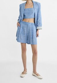 Set di due pezzi in misto lino blu chiaro, composto da un top corto con scollatura dritta e pantaloni corti sartoriali con pieghe. Da abbinare con ballerine color crema.