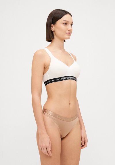 White wireless bra with a black elastic band featuring “Emporio Armani” logo, paired with tan bikini briefs with a matching waistband logo.
