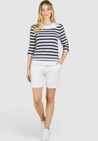 Gestreiftes Langarmhemd in Marineblau und Weiß, kombiniert mit weißen Shorts. Das Material wirkt weich und leicht. Frisches, lässiges Outfit mit Sneakers.