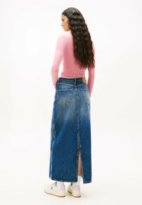 Gonna maxi in denim con spacco laterale, colore blu e texture sbiadita. Abbinata a una maglietta a maniche lunghe rosa e sneaker bianche.